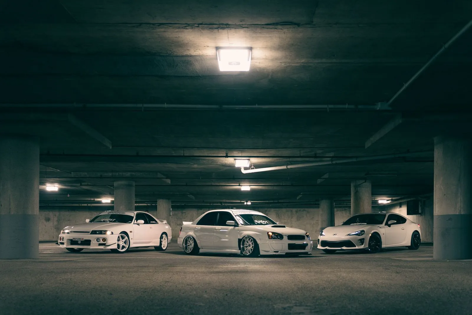 Three stylish white sports cars parked in a dimly lit underground garage, showcasing urban automotive elegance.